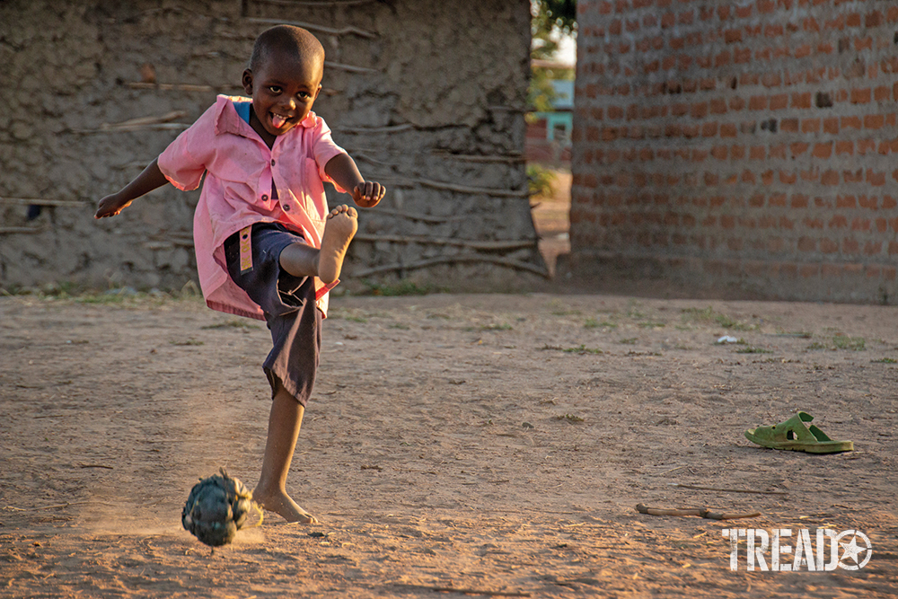 A Kenyan child in pink short and shorts plays soccer with plastic and twine ball. 