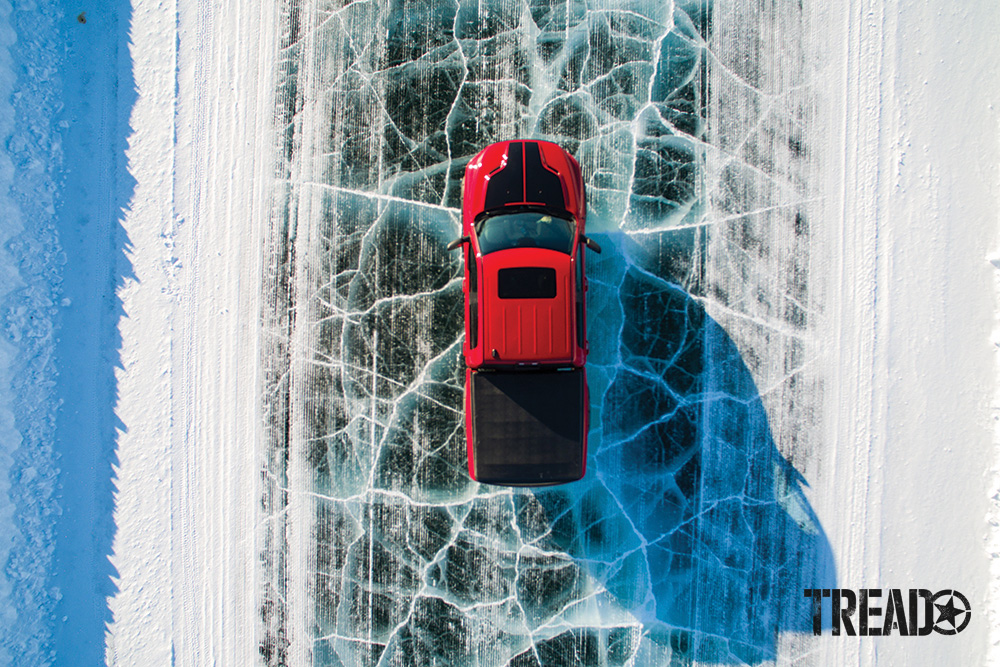 Shown in a bird's eye view, a red truck with black tonneau cover is driving on Arctic ice road.