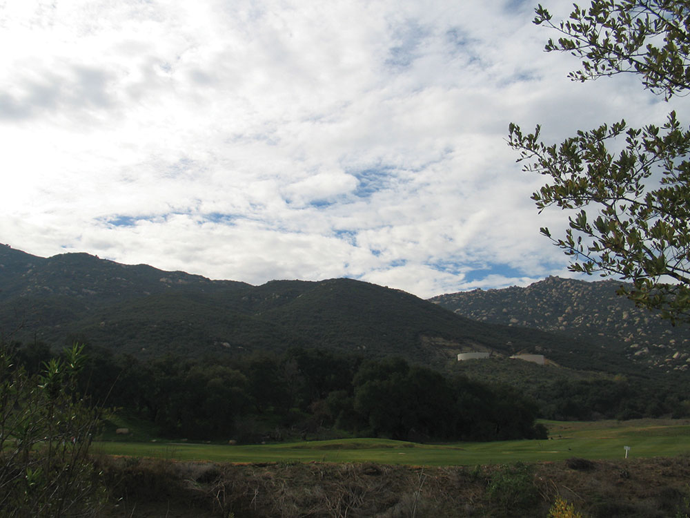 Dense Altostratus clouds over green mountains block out the sun.